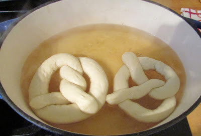 Dough shaped in pretzel twists getting baking soda water dunk.