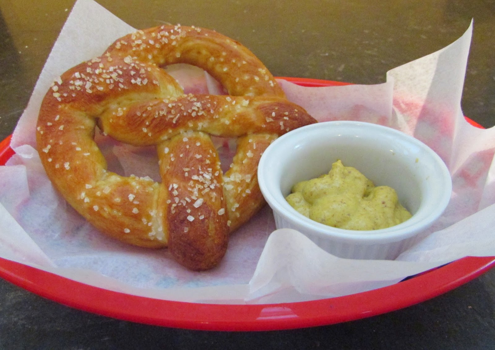 Homemade salty soft pretzel in basket with container of grainy mustard.