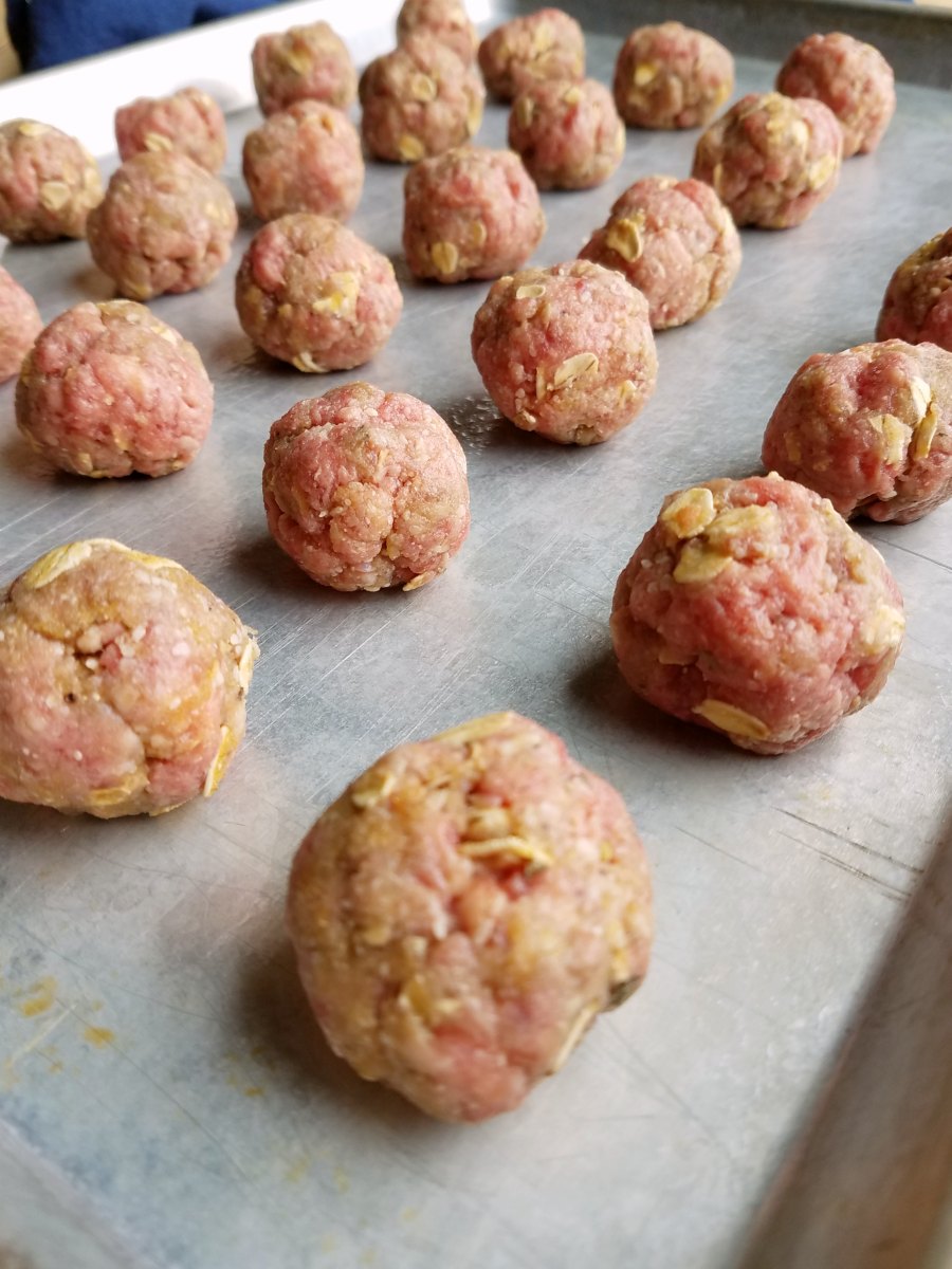 Sheet pan with rows of raw beef and oatmeal meatballs, ready to bake. 