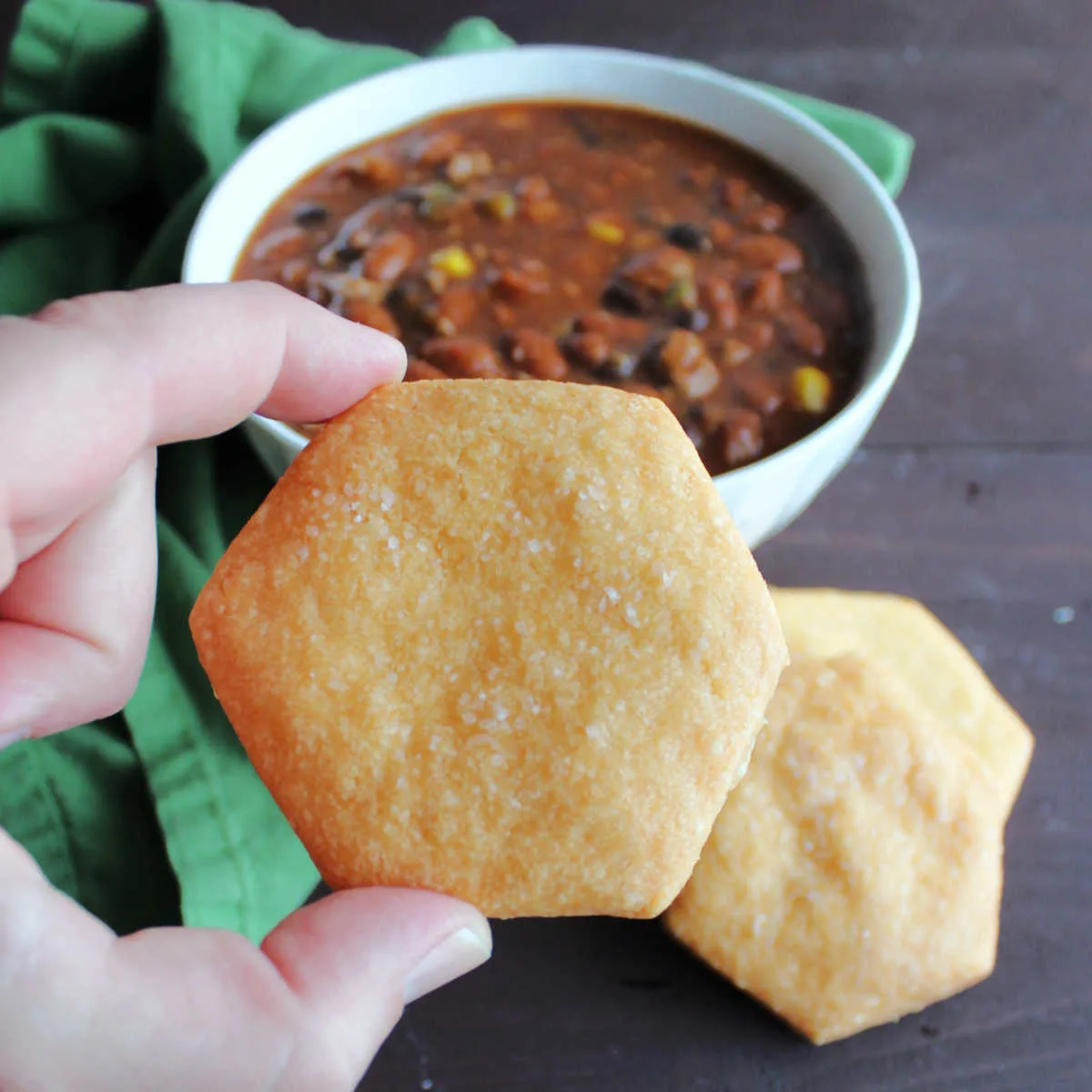 Hand holding cheese cracker in front of bowl of chili.