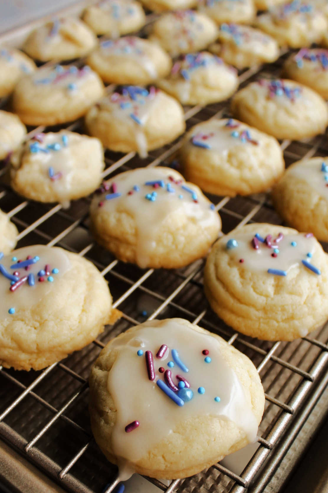 Soft sweetened condensed milk cookies with powdered sugar glaze and sprinkles on wire rack.