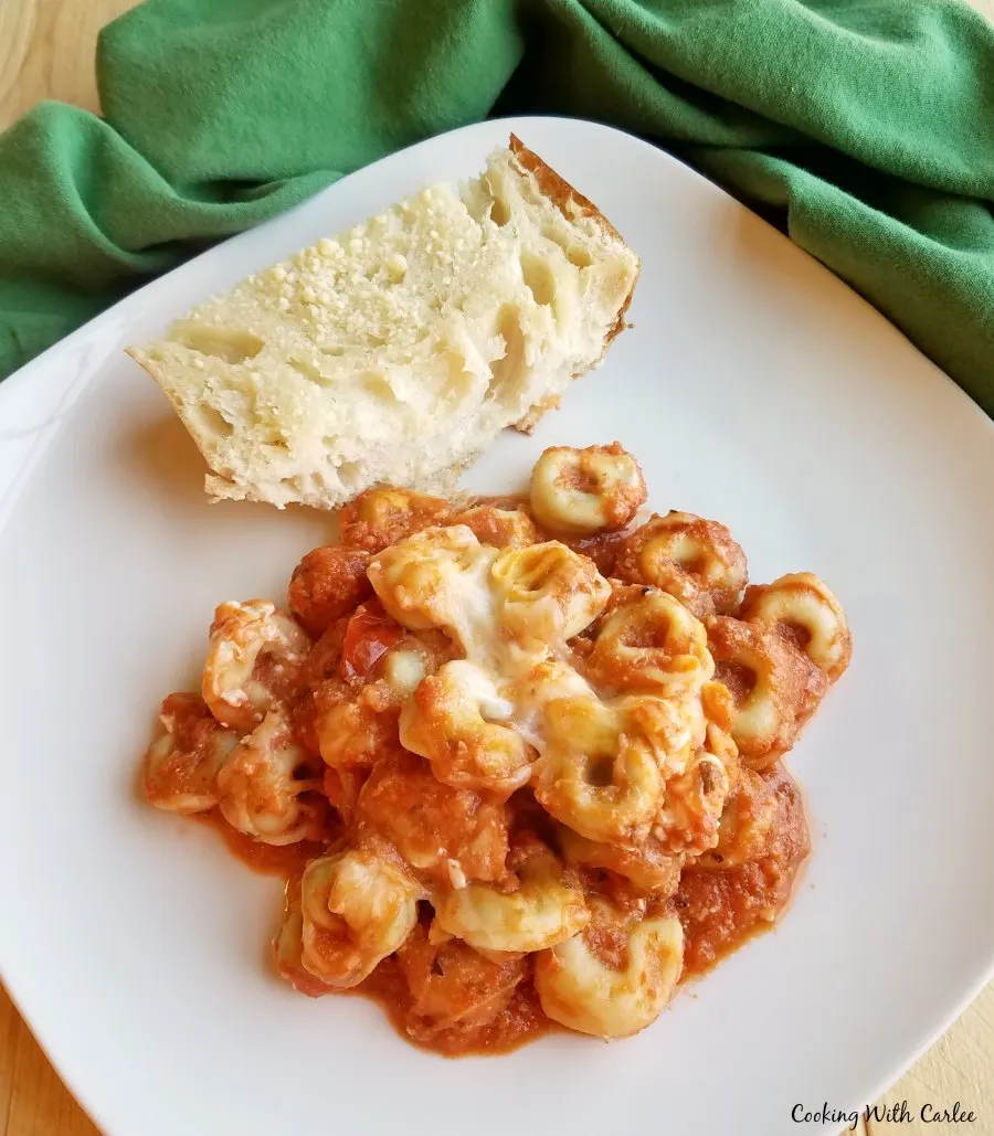 Plate of tortellini casserole with creamy tomato sauce and cheese on plate with hunk of garlic bread.