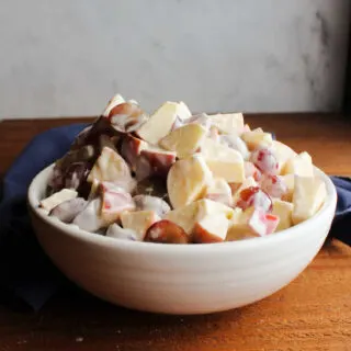 White serving bowl piled high with grape and apple salad dressed with a cinnamon and honey yogurt dressing.