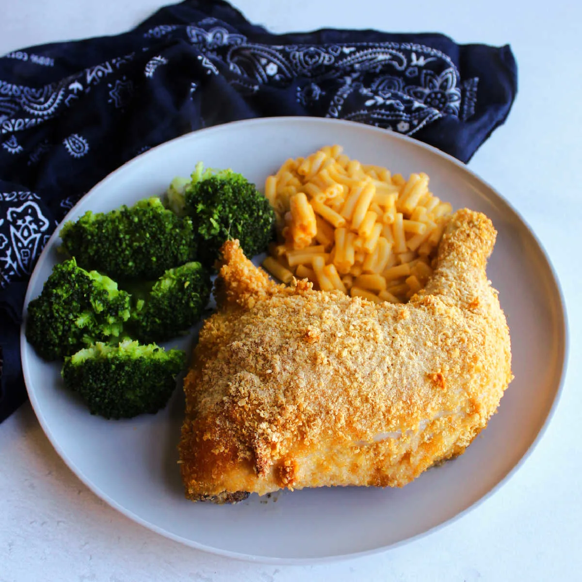 Dinner plate with cornflake crumb coated chicken leg quarter, mac and cheese and broccoli ready to eat.