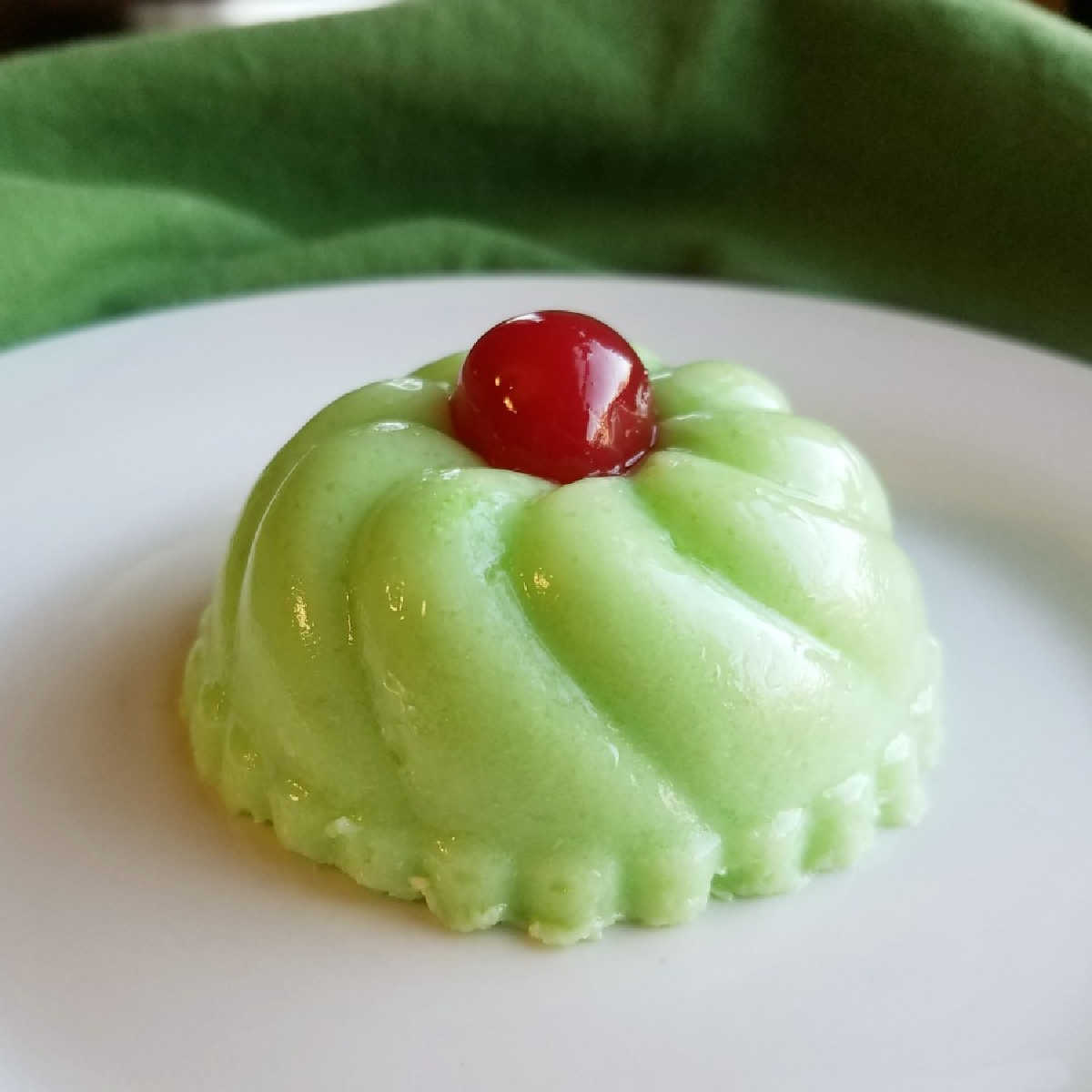 small green molded jello salad with maraschino cherry on top.