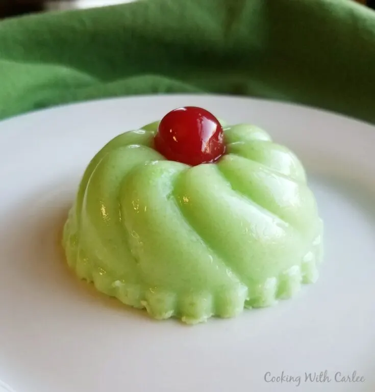 molded green jello salad with red maraschino cherry on top.