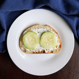 slice of italian bread topped with ranch cream cheese spread and slices of cucumber.