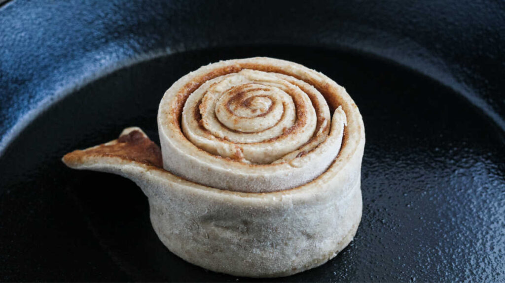 center of skillet cinnamon roll in middle of skillet with layers of cinnamon between layers of dough.