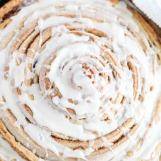 Close up of skillet full of large cinnamon roll with white glaze.