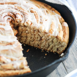 Cast iron skillet filled with giant cinnamon roll, with one slice missing showing all of the layers.