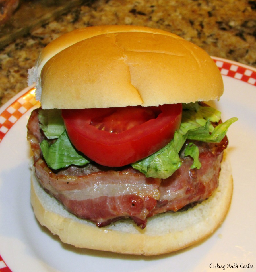 Stuffed burger wrapped with bacon on bun with lettuce and tomato.
