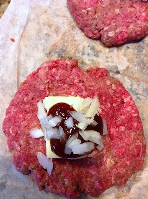 Ground beef patty topped with cheese, diced onions and bbq sauce ready for top patty to make stuffed hamburger surprises.