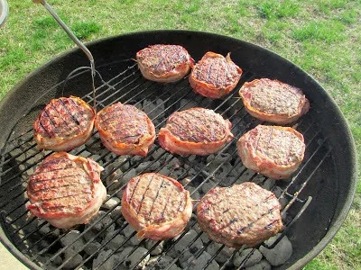 Bacon wrapped stuffed hamburgers on grill.