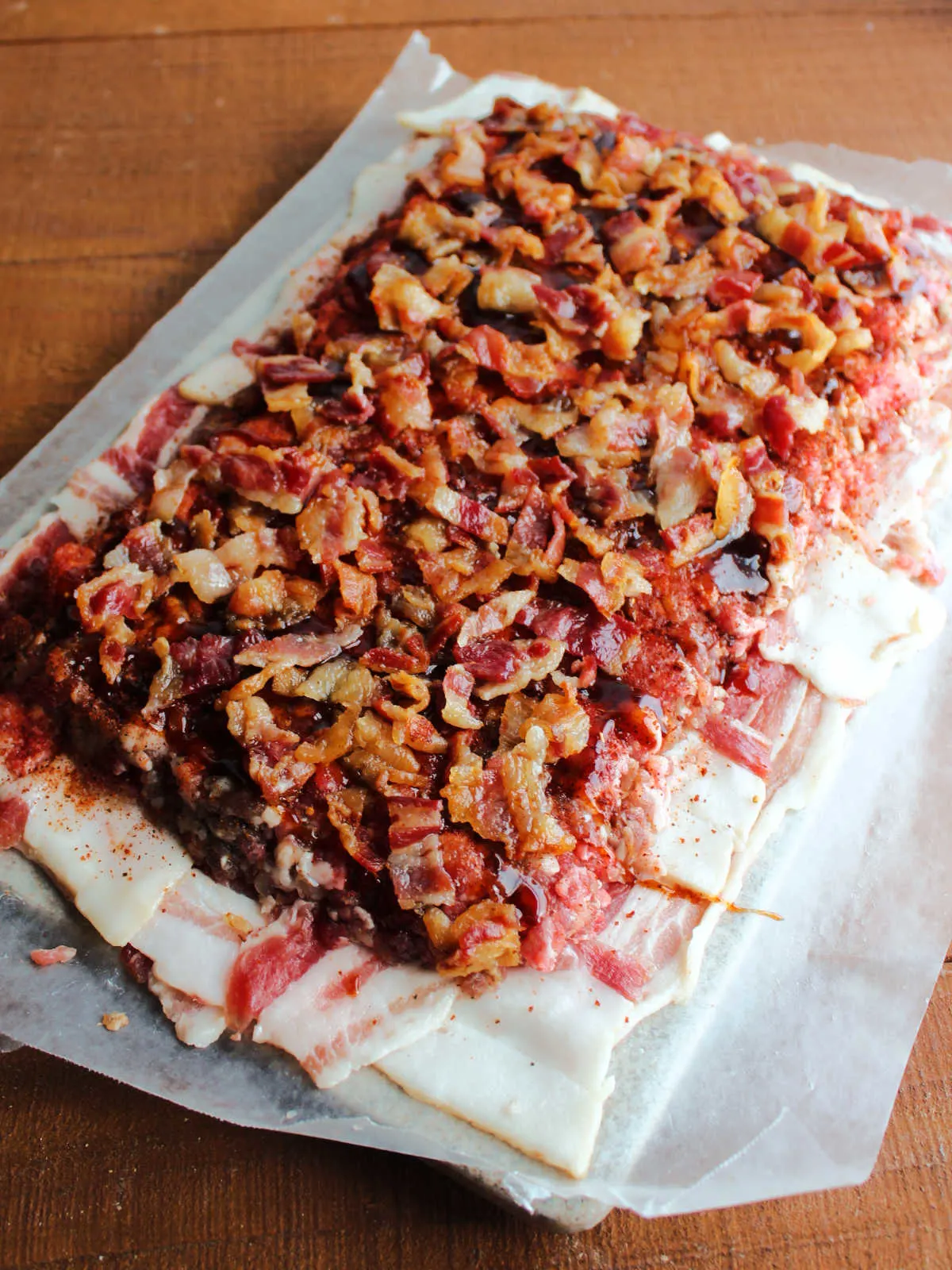Cooked and crumbled bacon spread over the top of the ground pork, ready to be rolled into the middle of the bacon fatty.