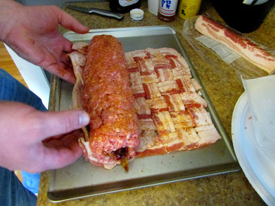 Ground meat rolled around the crumbled bacon center with hand getting ready to roll the bacon weave around the ground meat log. 