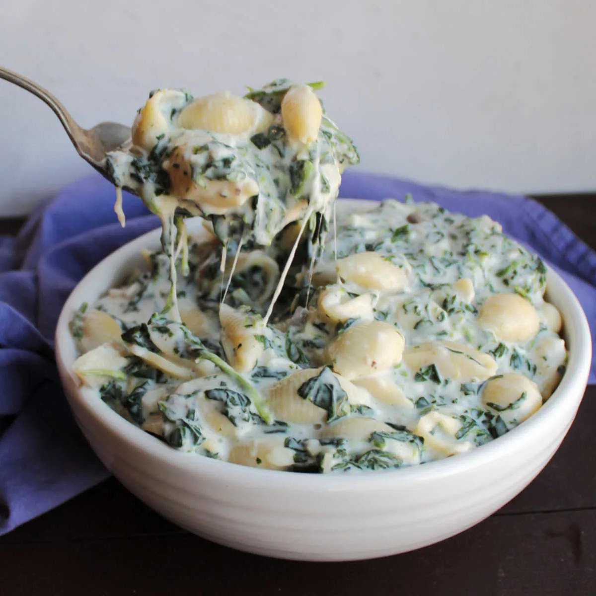 Serving spoon filled with creamy white mac and cheese with chopped spinach in it.