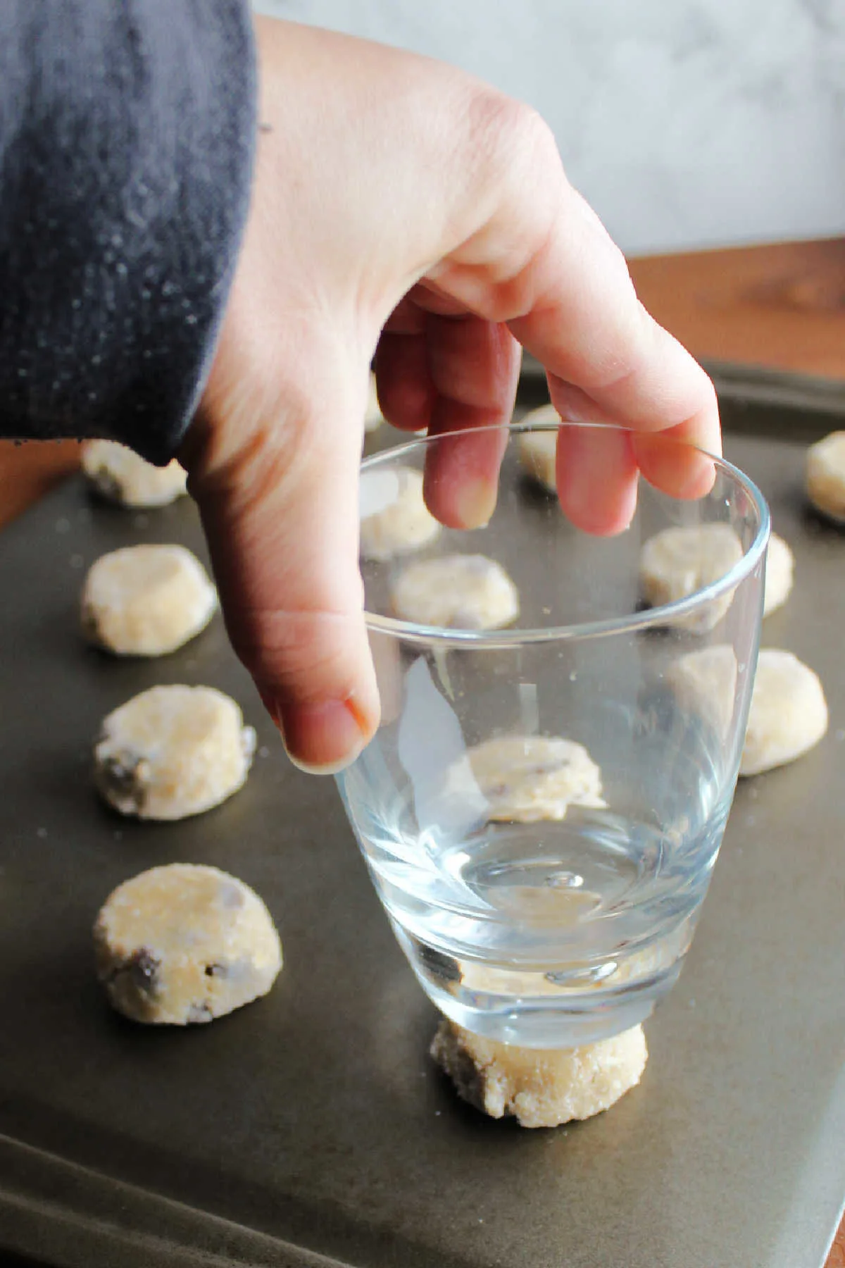 Flattening refrigerated balls of oatmeal raisin cookie dough with the bottom of a glass.