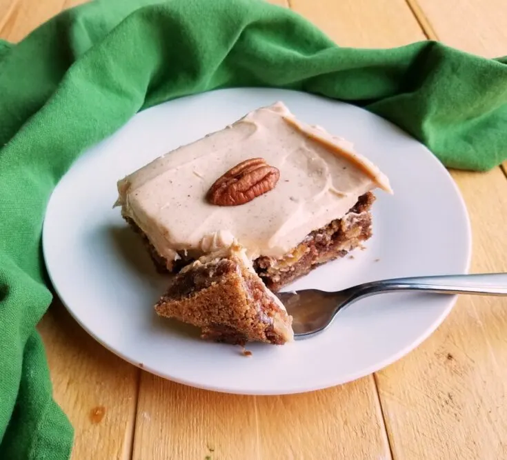 piece of german apple cake on plate with light brown cinnamon cream cheese frosting and a pecan half on top