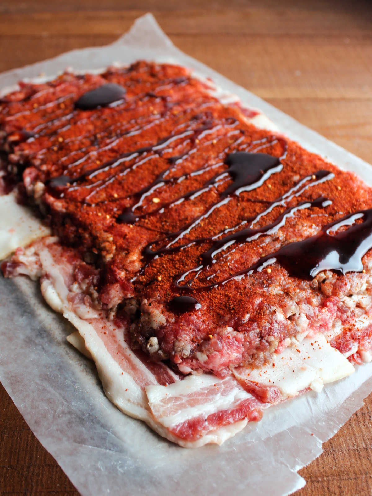 Ground pork and sausage mixture patted into a rectangle on top of the bacon weave then topped with BBQ rub and a drizzle of BBQ sauce.