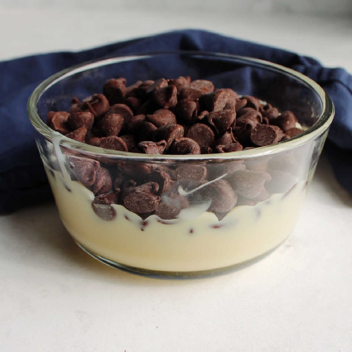 Chocolate chips and condensed milk in small glass bowl.