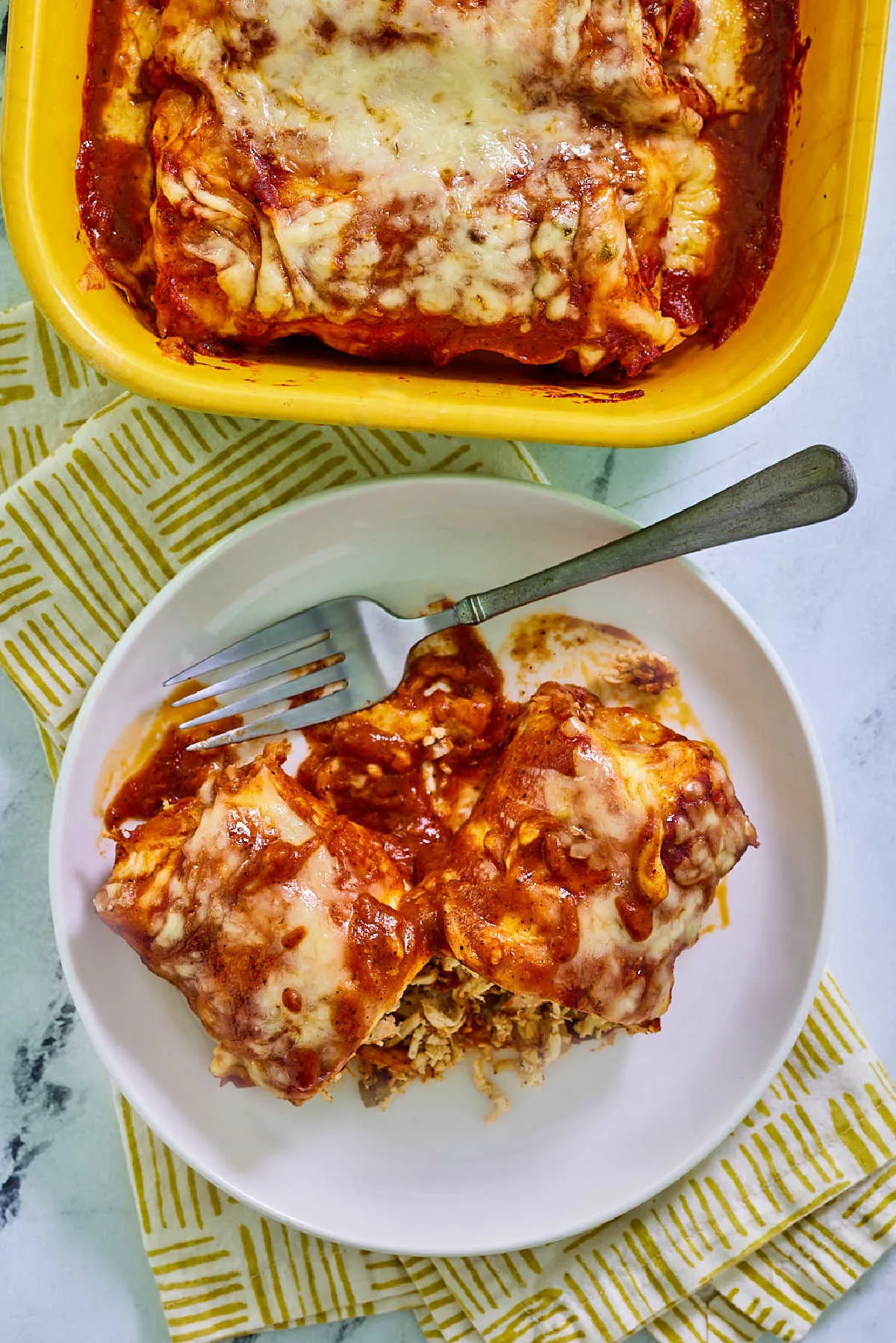 Chicken enchilada with homemade red sauce and melted cheese on plate with fork, ready to eat. 