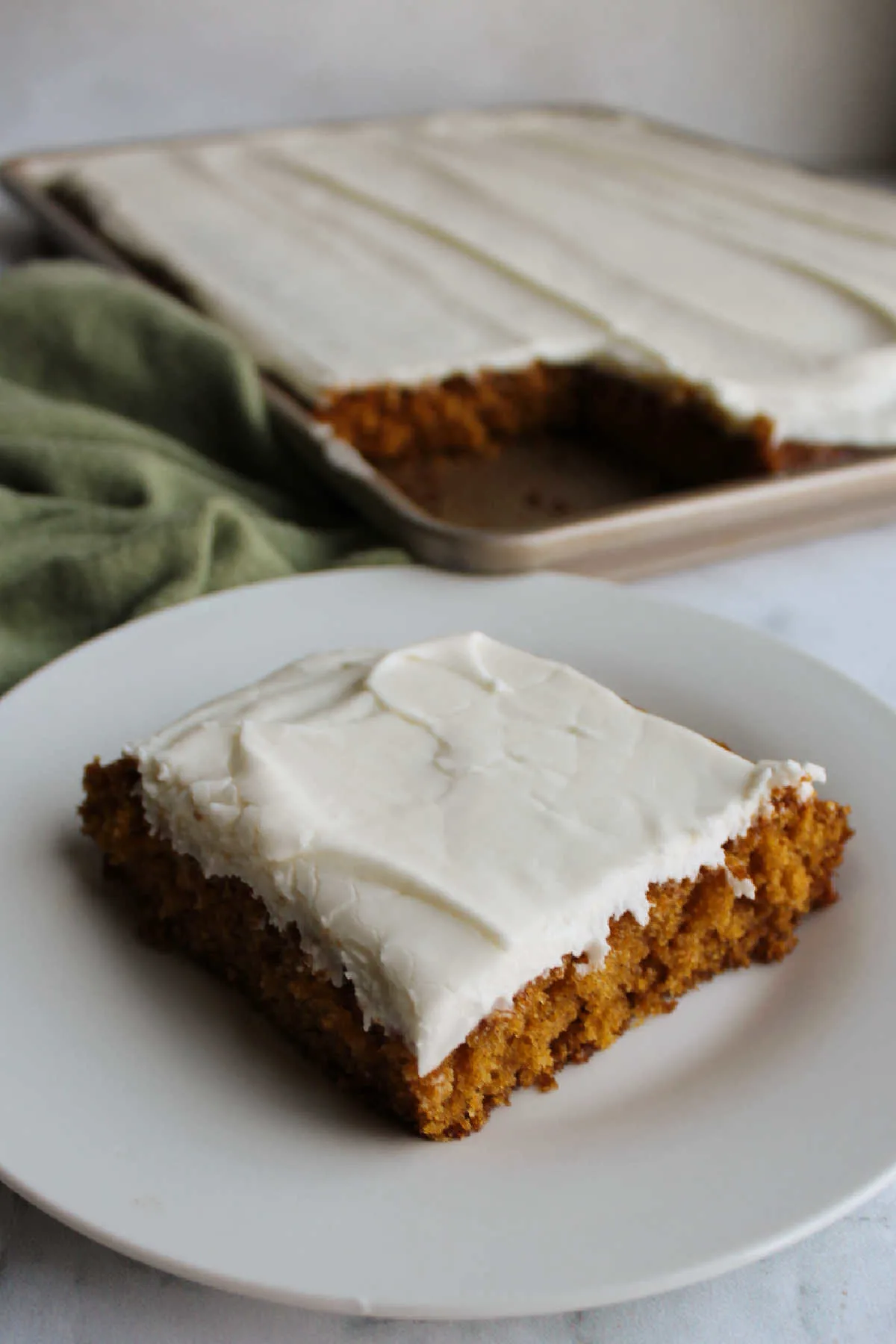 Frosted pumpkin bar on plate in front of pan of remaining bars. 