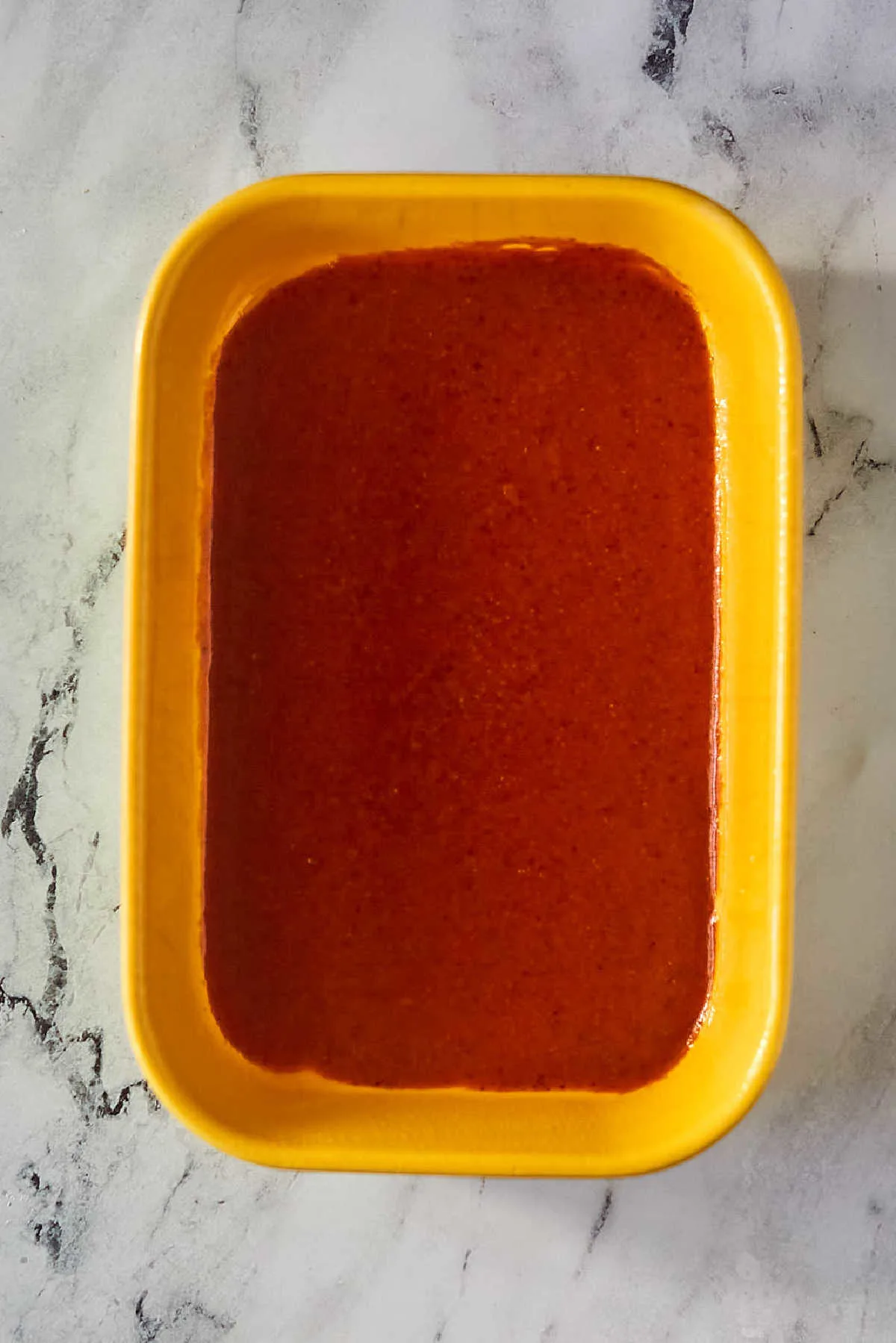 Red enchilada sauce in bottom of pan, ready for enchiladas. 