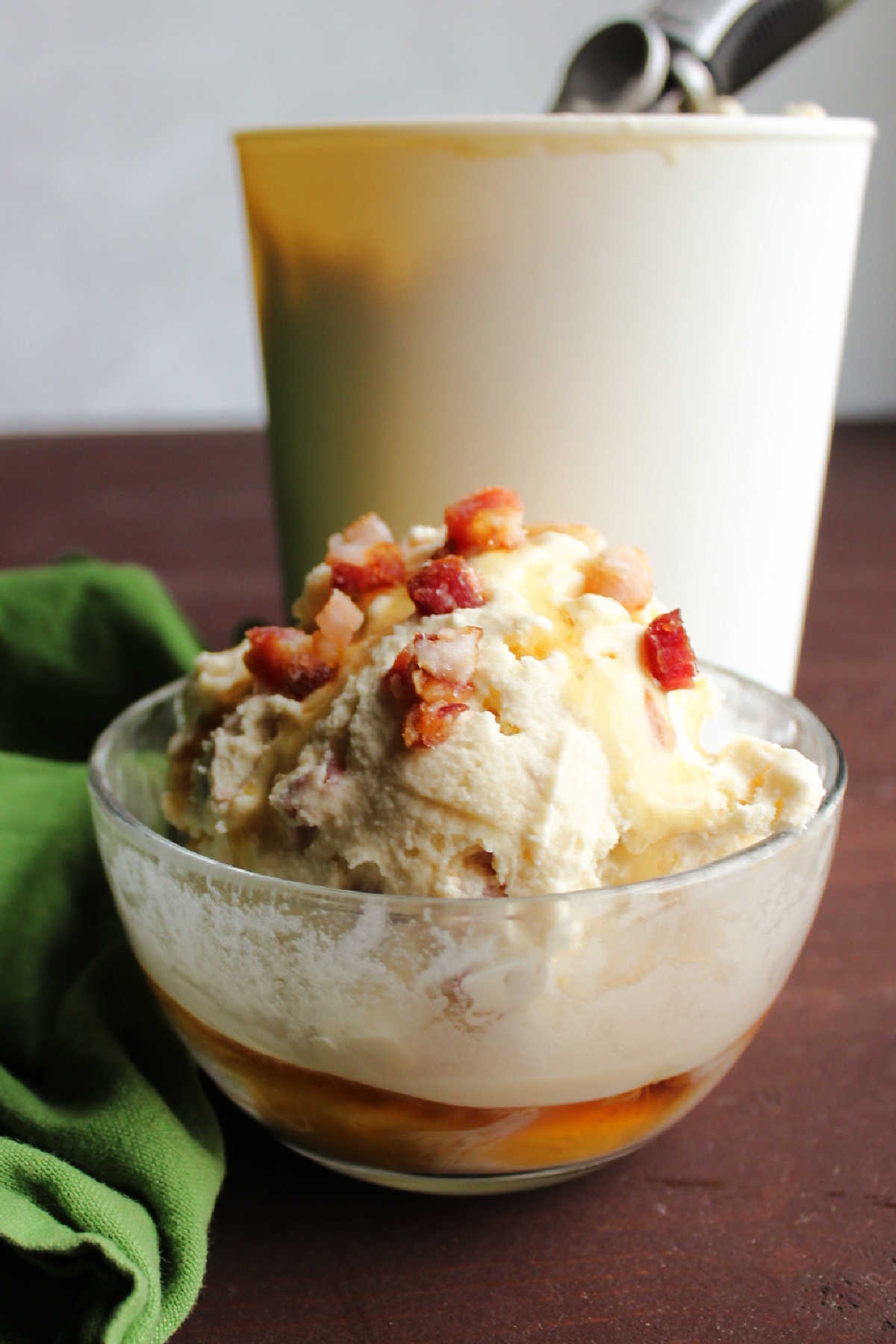 Looking across bowl of maple bacon ice cream topped with bits of crisp bacon and extra maple syrup.