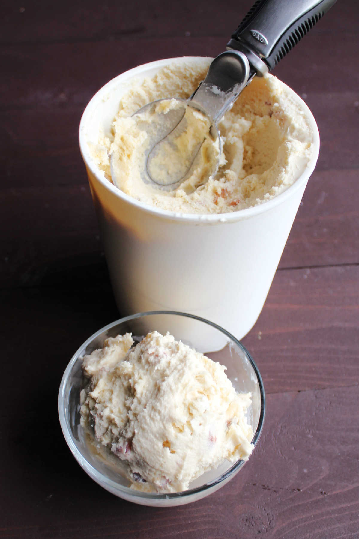 scoop of maple bacon ice cream in small glass bowl in front of storage container.