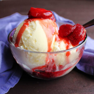 scoops of homemade vanilla ice cream topped with strawberry sauce.