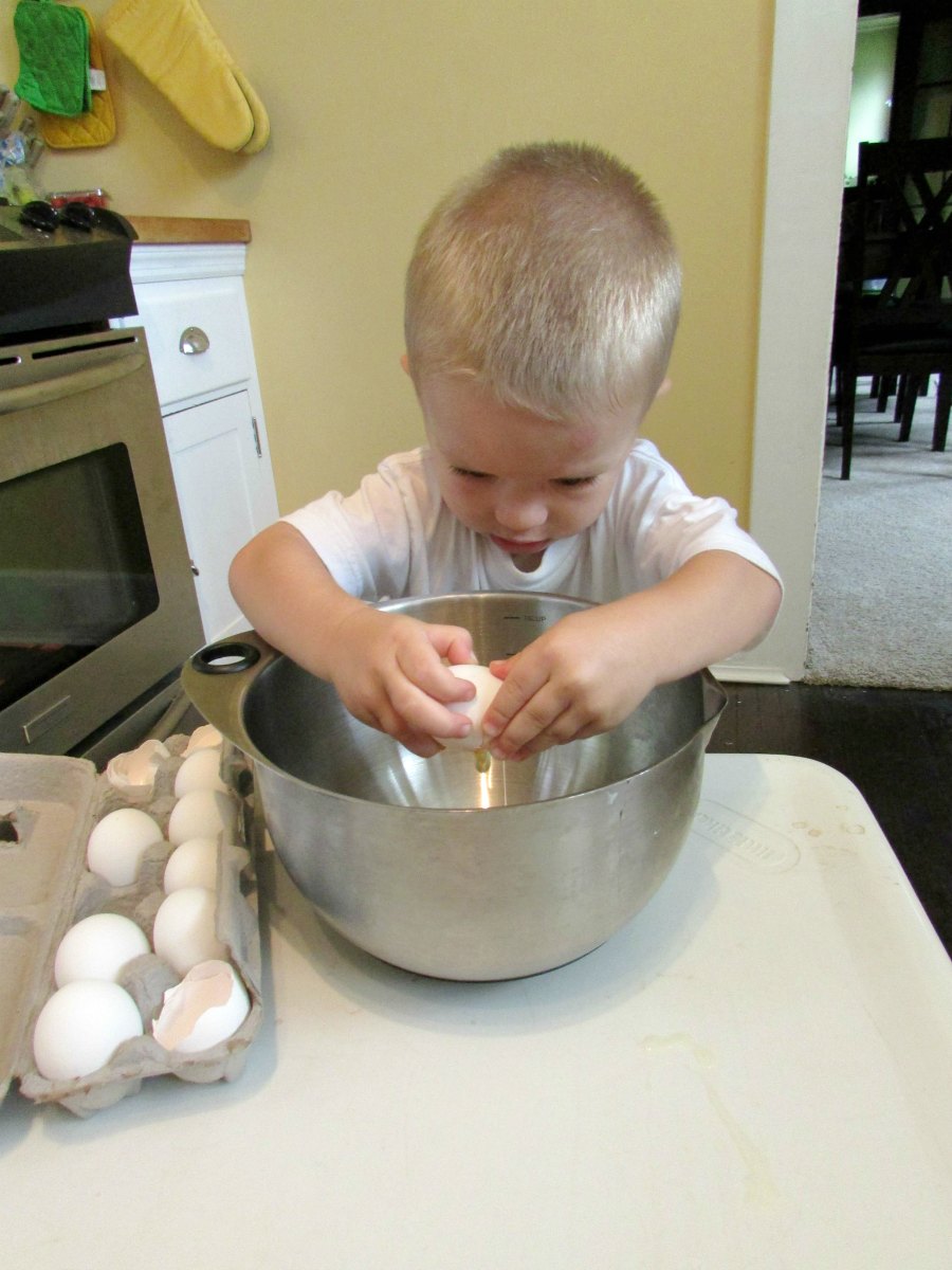 Small child cracking eggs into mixing bowl. 