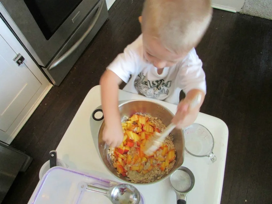 Small child stealing pieces of peach out of mixing bowl.