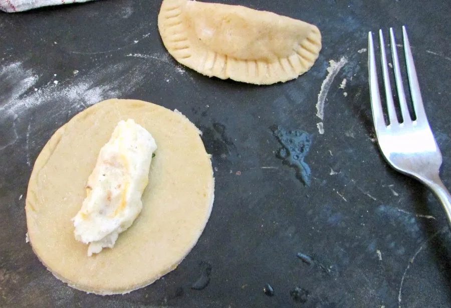 Fork sealing pierogi dough around mashed potato filling.