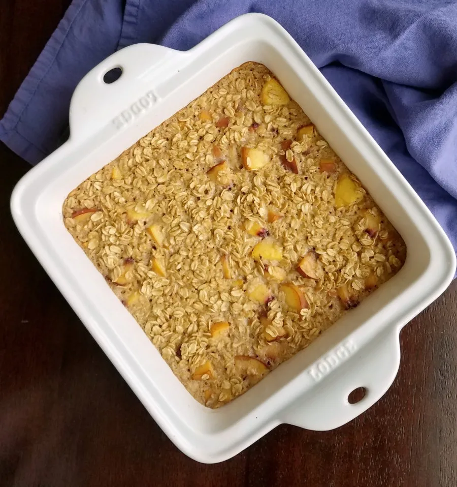 Square baking dish filled with freshly baked peaches and cream baked oatmeal.