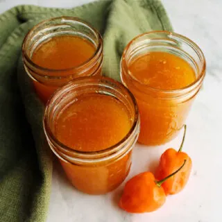 Jars of freshly made habanero peach jelly with orange habaneros nearby.
