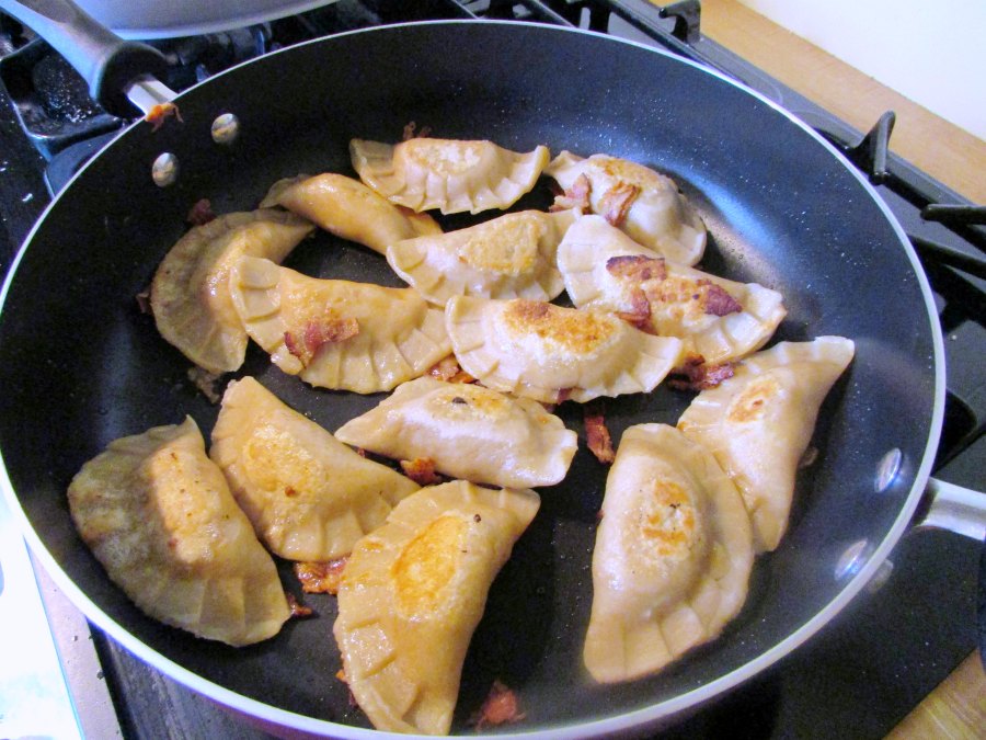 Browning boiled pierogi in large skillet with bits of bacon.