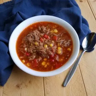 Bowl of brunswick stew with leftover bbq meat, corn and tomatoes in bowl with spoon.