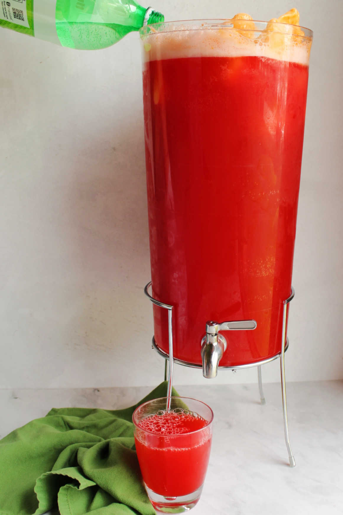 Pouring ginger ale into beverage dispenser filled with colorful punch and orange sherbet.