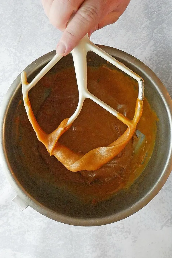 Hand holding mixer paddle with caramel frosting on it.