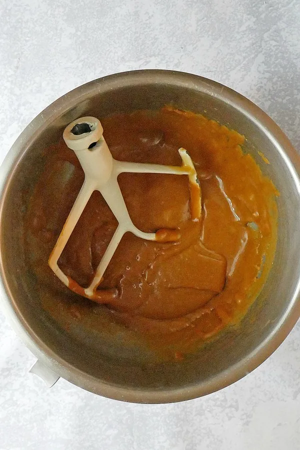Mixer bowl of caramel frosting with paddle, ready for cake.