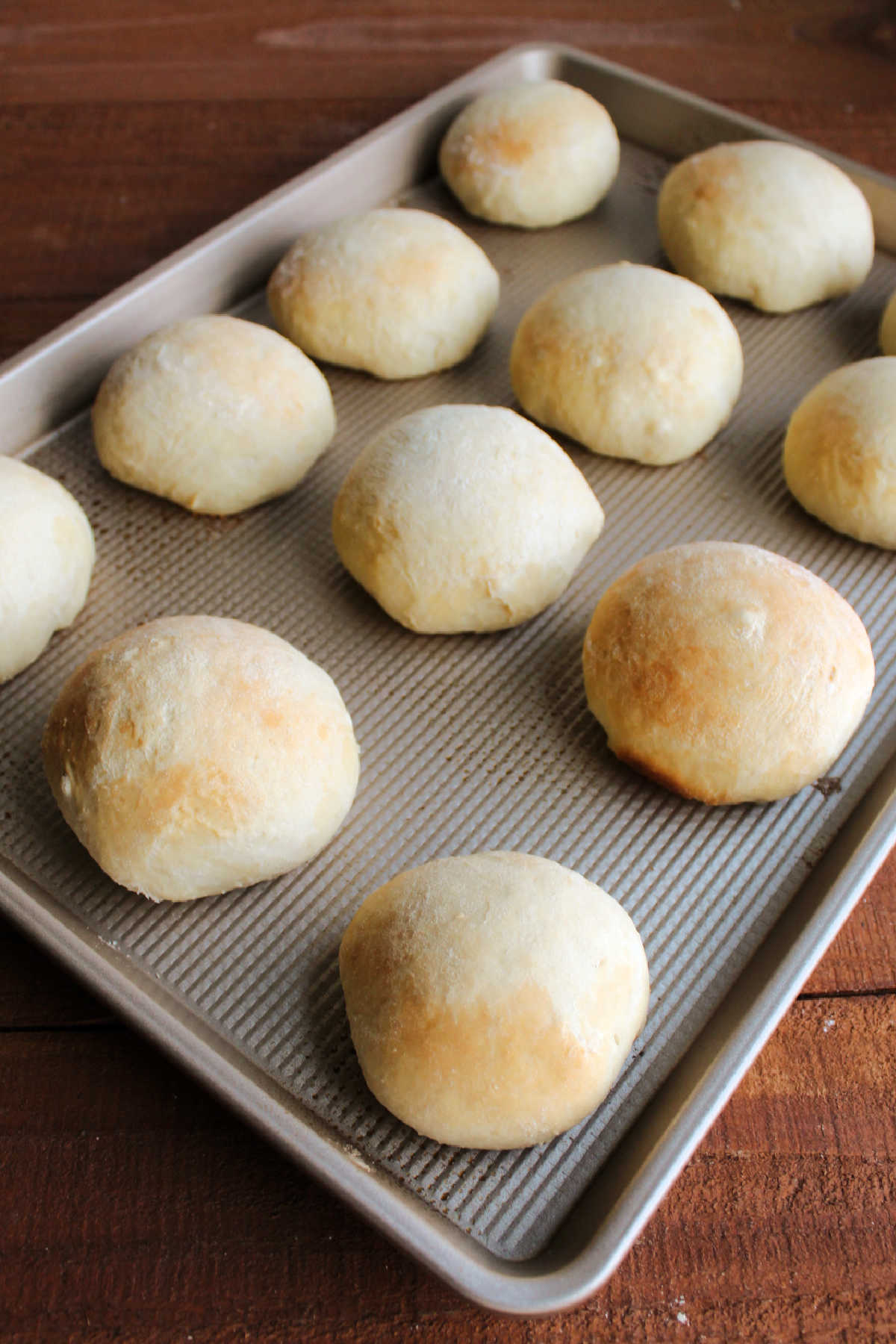 Freshly baked rolls with light golden brown tops on sheet pan.