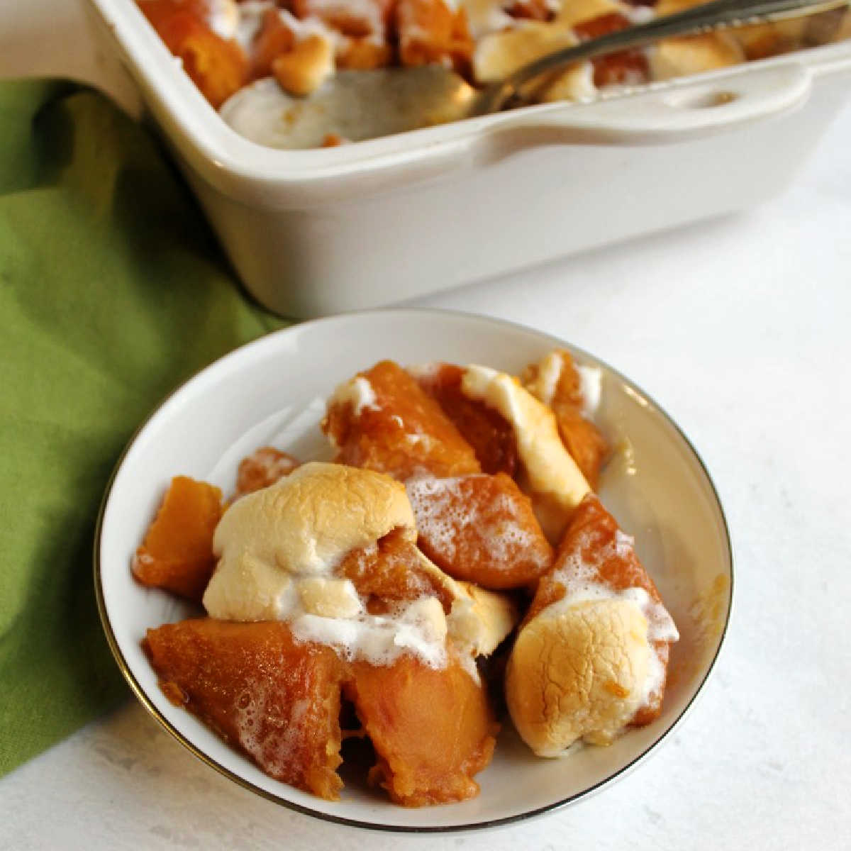 small dish of candied sweet potatoes with marshmallows in front of remaining pan.