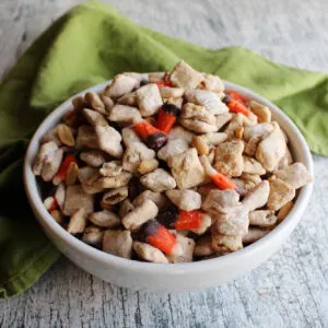 Bowl of fall puppy chow mix with white chocolate muddy buddies, candy corn, and peanuts.