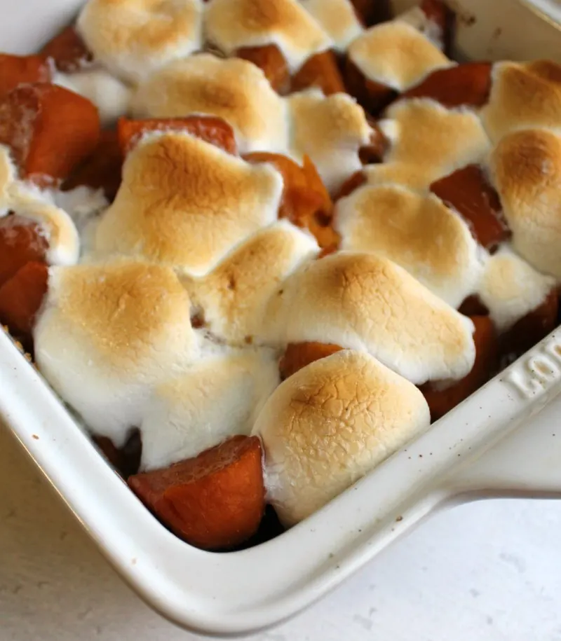 corner of pan filled with candied sweet potatoes topped with golden brown gooey marshmallows. 