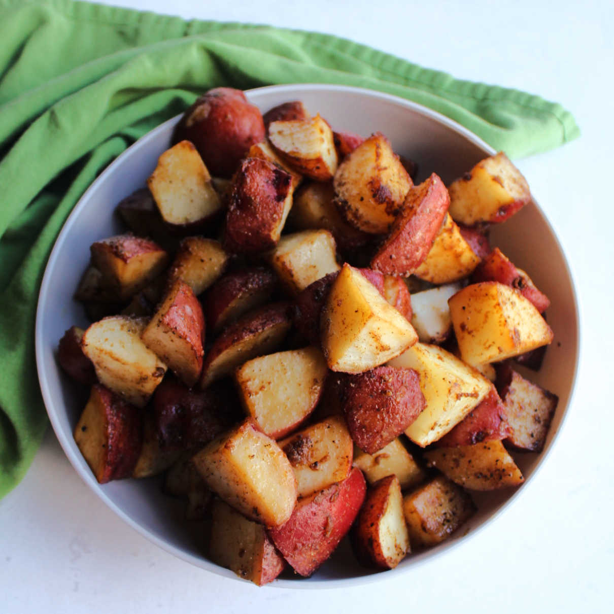 Serving bowl filled with chunks of roasted red skin potatoes coated in seasonings, ready to eat.