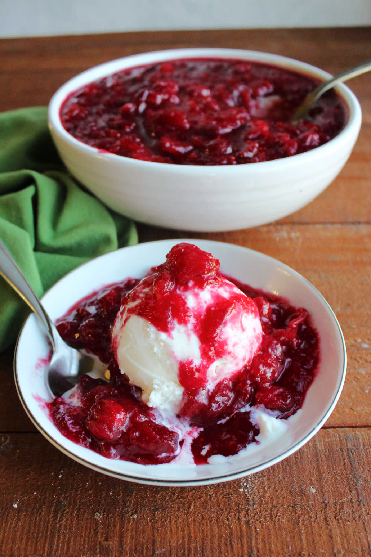 Warm cranberry sauce spooned over scoop of vanilla ice cream in a small bowl.