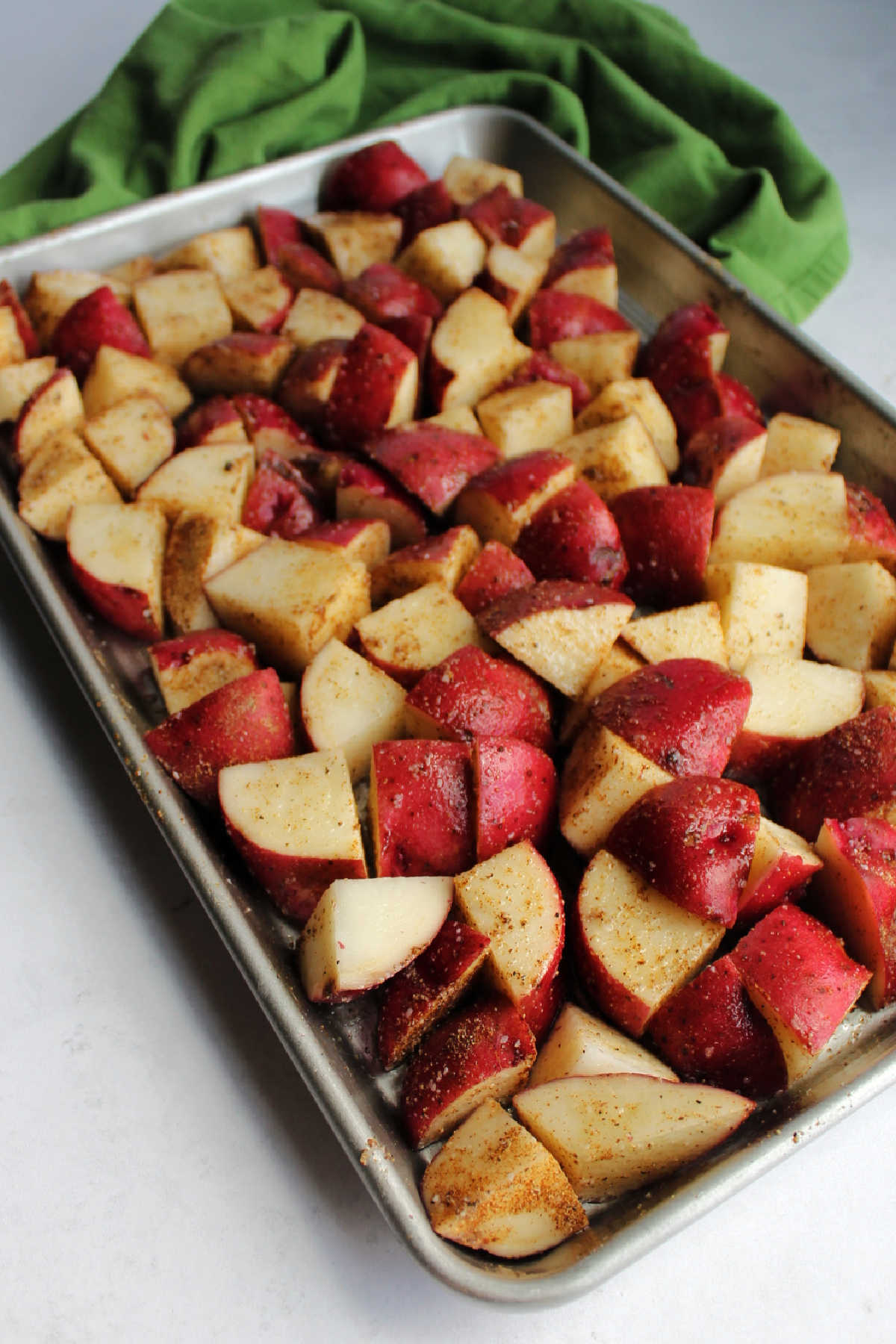 Chunks of red skin potato tossed in oil and seasonings on baking sheet ready to go in the oven.