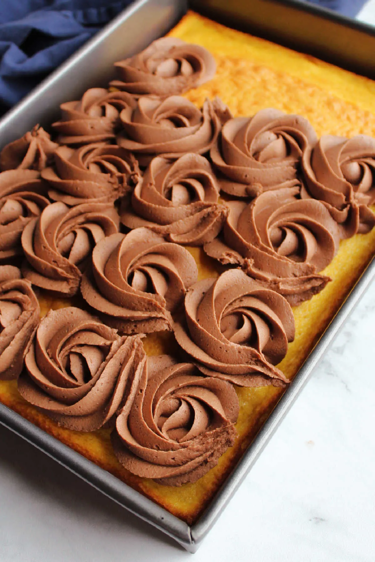 Rosettes of chocolate brownie batter frosting piped onto sheet cake.