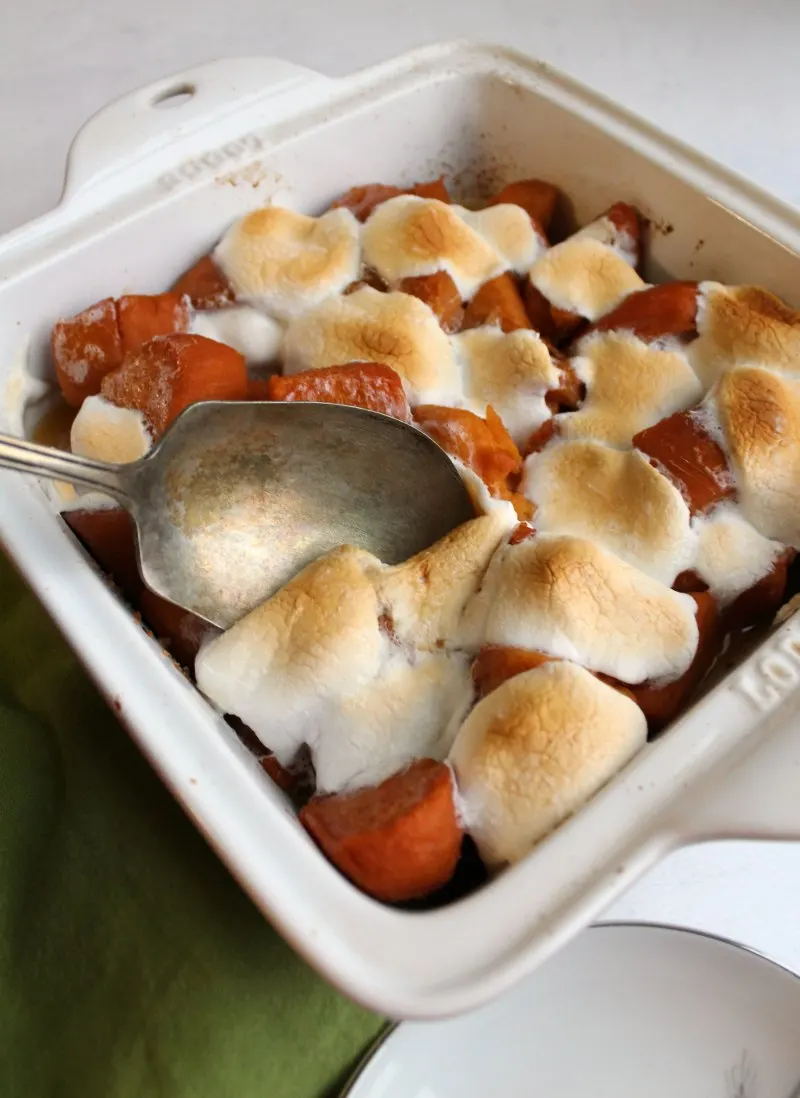 Spoon dipping into pan of marshmallow topped candied sweet potatoes. 