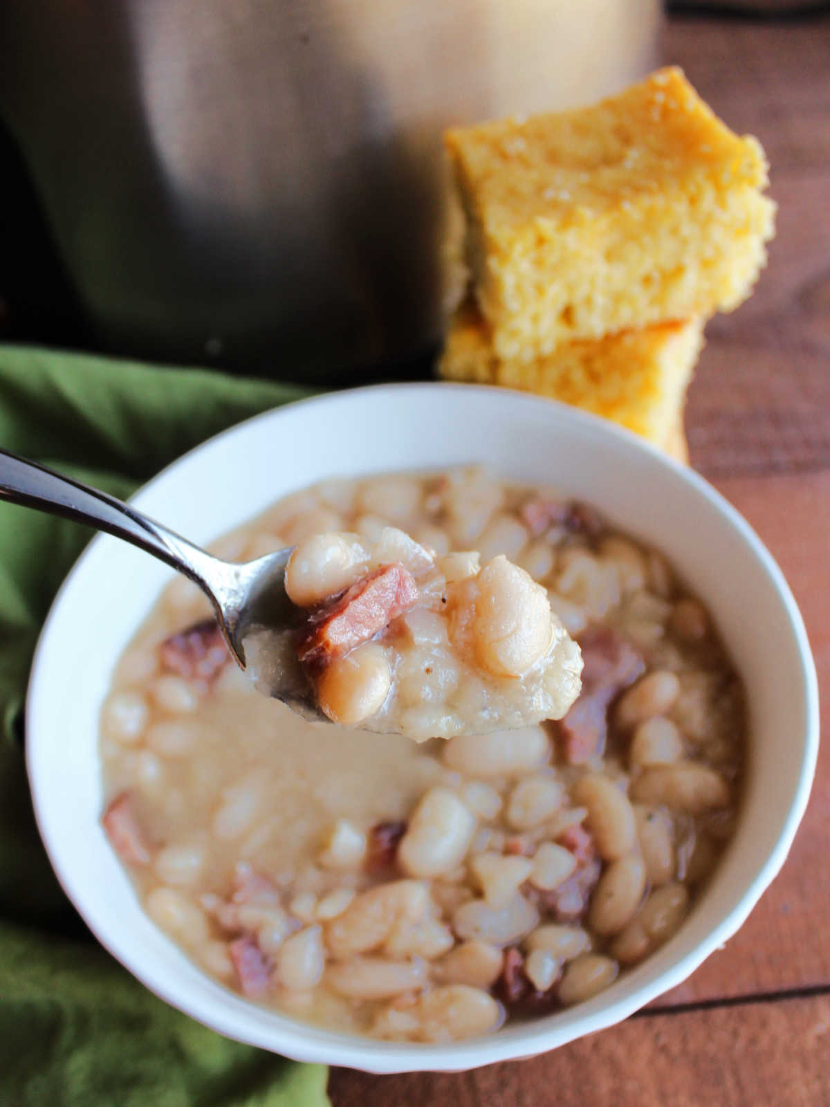 Spoonful of ham and beans with cornbread and crockpot in the background.